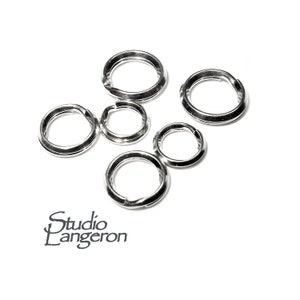 以下が含まれることがあります： 白い背景に、さまざまなサイズの銀色の丸カンがいくつかあります。これらの開いたリングは、ジュエリー作りや工芸品向けです。Studio Langeronのロゴが左下に表示されています。