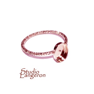 Pode incluir: Um anel em ouro rosa com uma banda texturizada e uma moldura redonda. O anel está sobre um fundo branco. O texto "Studio Langeron" está no canto inferior esquerdo.
