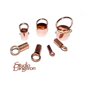 Peut inclure: Divers éléments de bijouterie de couleur cuivre, dont de petits capuchons cylindriques avec des boucles et de petits composants en forme de seau avec des poignées. Le logo Studio Langeron est visible en bas à gauche.