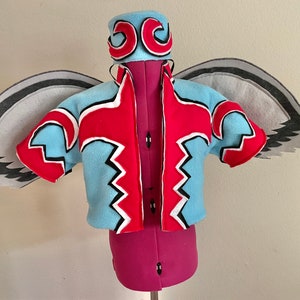 May include: A blue and red costume with a black and white geometric pattern. The costume includes a hat with a black and white geometric pattern and wings with a gray and black pattern.
