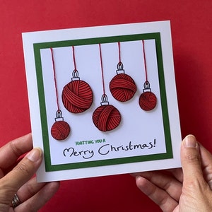 May include: A white card with a green border and a red and white yarn ball ornament design. The card says "Knitting you a Merry Christmas!"