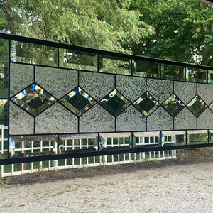 Pu&ograve; includere: Una finestra in vetro colorato con un design geometrico che presenta vetro trasparente con una finitura testurizzata e cames in piombo nero. La finestra &egrave; appesa a una cornice in metallo nero.