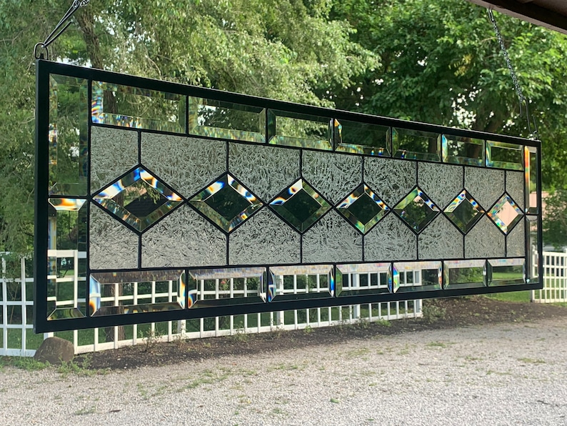 Pu&ograve; includere: Una finestra in vetro colorato con un design geometrico che presenta vetro trasparente con una finitura testurizzata e cames in piombo nero. La finestra &egrave; appesa a una cornice in metallo nero.