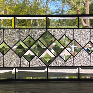Op de afbeelding: Een glas-in-loodraam met een geometrisch ontwerp met heldere glazen diamanten in een textuurrijke glazen achtergrond.