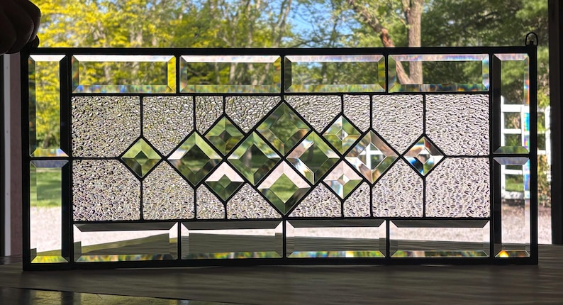 Op de afbeelding: Een glas-in-loodraam met een geometrisch ontwerp met heldere glazen diamanten in een textuurrijke glazen achtergrond.