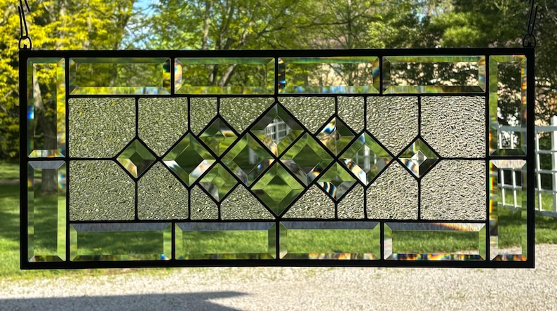 Op de afbeelding: Een glas-in-loodraam met een ruitpatroon. Het glas is helder en heeft een textuur. Het raam is omlijst met zwart.