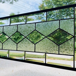 Pu&ograve; includere: Un pannello di vetro colorato con un design geometrico con vetro trasparente e verde. Il pannello &egrave; incorniciato in metallo nero.