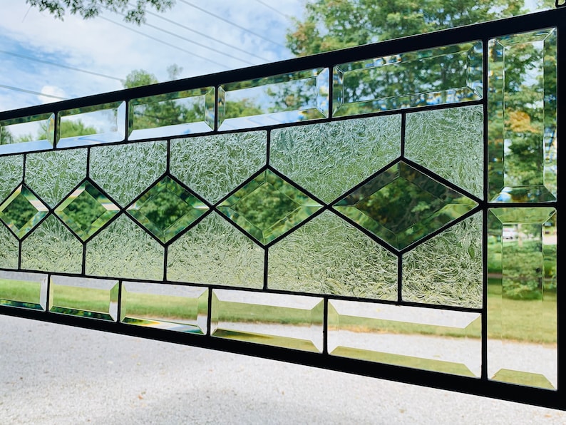 Pu&ograve; includere: Un pannello di vetro colorato con un design geometrico con vetro trasparente e verde. Il pannello &egrave; incorniciato in metallo nero.