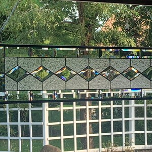 Pu&ograve; includere: Un pannello di vetro colorato con un design geometrico che presenta una fila di forme a diamante in vetro trasparente con accenti iridescenti. Il pannello della finestra &egrave; incorniciato in nero.