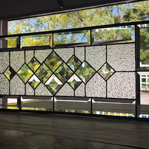 Op de afbeelding: Een glas-in-loodraam met een ruitvormig patroon. Het glas is helder met een getextureerd oppervlak. Het raam is omlijst met zwart metaal.