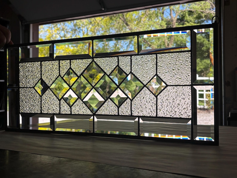 Op de afbeelding: Een glas-in-loodraam met een ruitvormig patroon. Het glas is helder met een getextureerd oppervlak. Het raam is omlijst met zwart metaal.