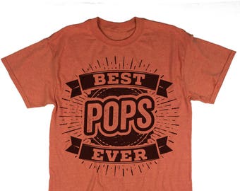 Könnte beinhalten: Orangefarbenes T-Shirt mit einer abgenutzten braunen Grafik, auf der in einem Kreis mit einem Banner "Best Pops Ever" steht.