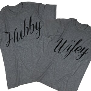 Puede incluir: Dos camisetas grises con las palabras "Hubby" y "Wifey" impresas en fuente cursiva negra.
