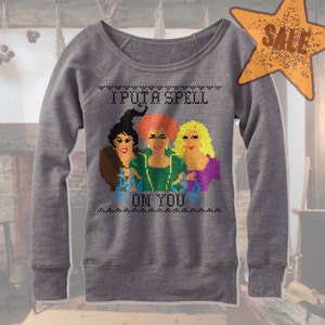 May include: Gray sweatshirt with a pixelated design featuring three witches and the phrase "I Put a Spell on You." The design includes the witches with black, red, and yellow hair. A star-shaped "SALE" graphic is in the upper right corner.