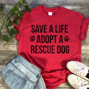 May include: Red t-shirt with the text "Save a life adopt a rescue dog" in black with two paw prints on either side of the word "adopt".