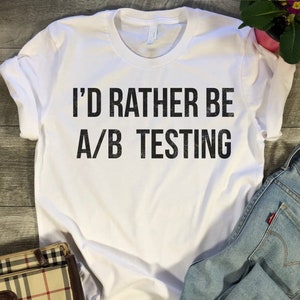 May include: White t-shirt with the text "I'd rather be A/B testing" printed in black.