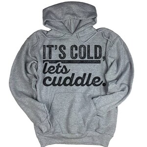 May include: Gray hooded sweatshirt with the text "It's cold, lets cuddle." printed in black.