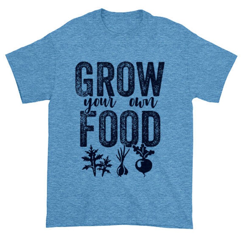 May include: A light blue t-shirt with the text "Grow your own food" in a dark blue distressed font. The text is surrounded by images of various vegetables, including a beet, a garlic bulb, and two leafy greens.