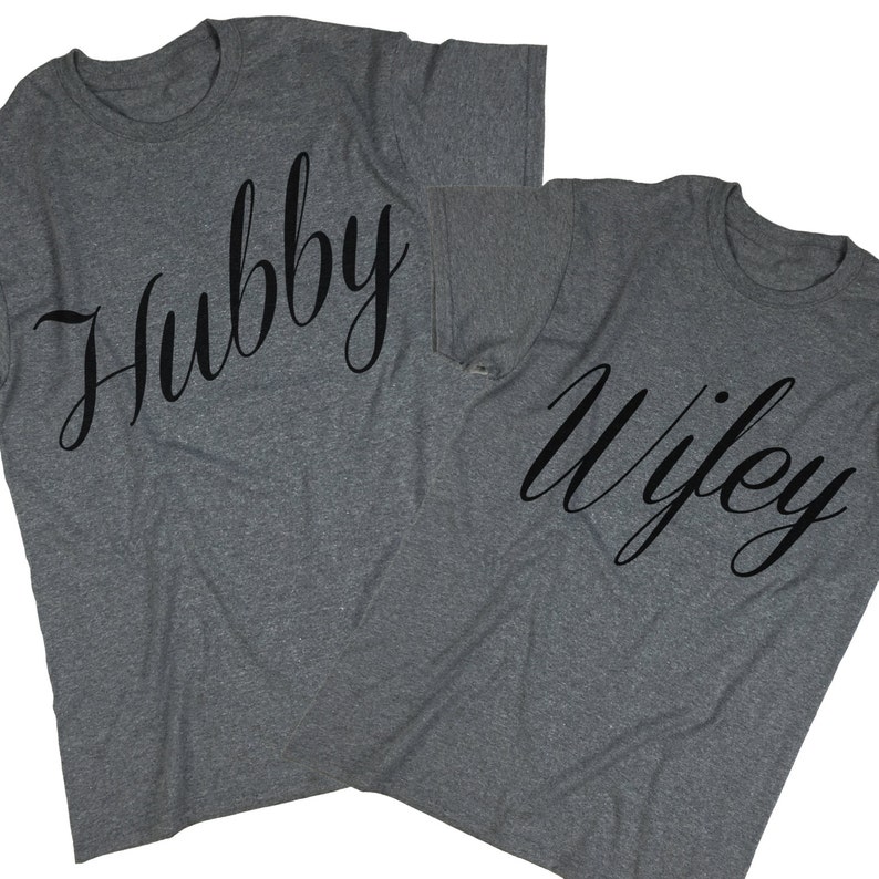 Puede incluir: Dos camisetas grises con las palabras "Hubby" y "Wifey" impresas en fuente cursiva negra.