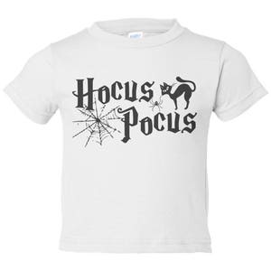 K&ouml;nnte beinhalten: Wei&szlig;es T-Shirt f&uuml;r Kleinkinder mit einem schwarzen Aufdruck einer Katze, einer Spinne und einem Spinnennetz mit dem Text "Hocus Pocus".