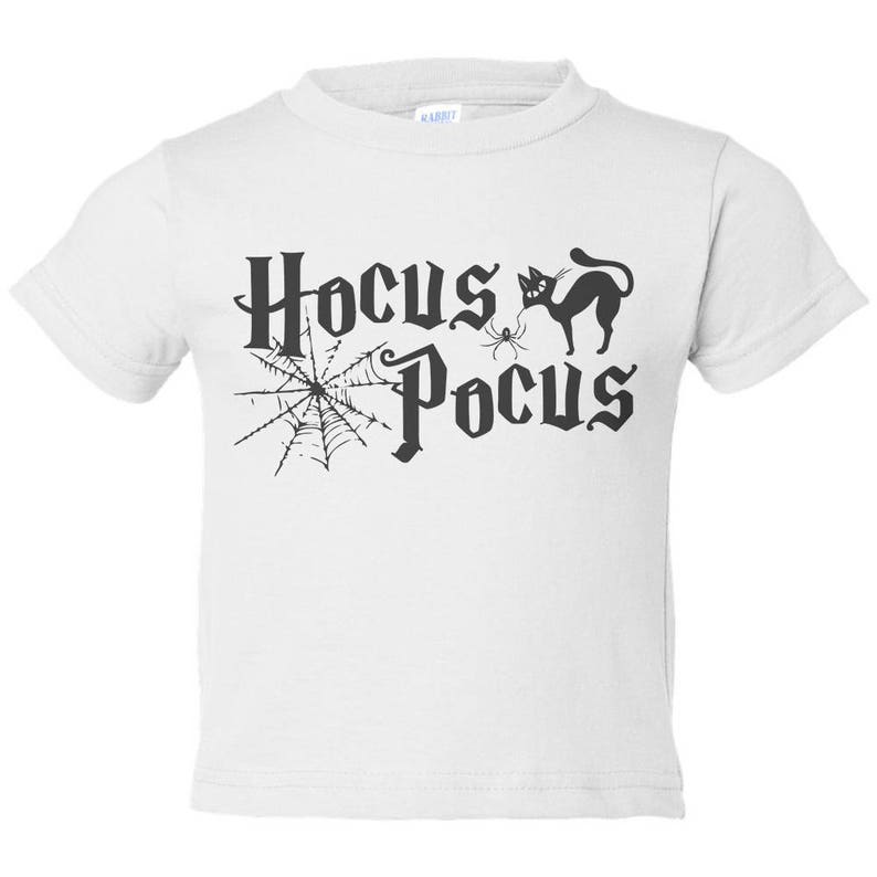 K&ouml;nnte beinhalten: Wei&szlig;es T-Shirt f&uuml;r Kleinkinder mit einem schwarzen Aufdruck einer Katze, einer Spinne und einem Spinnennetz mit dem Text "Hocus Pocus".
