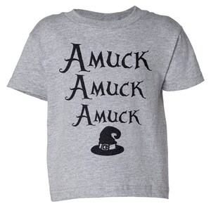 Pu&ograve; includere: Una maglietta grigio melange con le parole "Amuck Amuck Amuck" in corsivo nero e una grafica di cappello da strega nero. La maglietta &egrave; a girocollo e maniche corte.