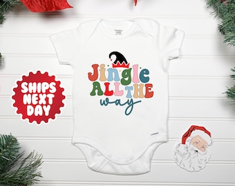 Könnte beinhalten: Weißer Baby-Strampler mit einer bunten Grafik im Retro-Stil, auf der "Jingle All The Way" steht. Die Grafik enthält eine rot-weiße Elfenmütze.