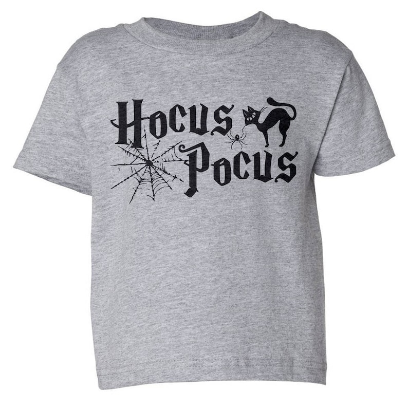 K&ouml;nnte beinhalten: Ein graues T-Shirt mit kurzen &Auml;rmeln mit dem Text "Hocus Pocus" in Schwarz, mit einer schwarzen Katze und einem Spinnennetz.