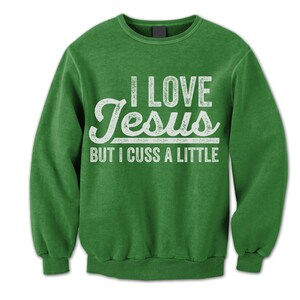 May include: Green sweatshirt with a white distressed graphic that reads "I Love Jesus But I Cuss A Little."