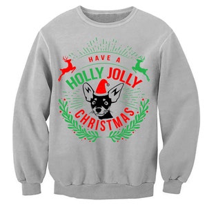 May include: A grey sweatshirt with a Christmas design featuring a black and white dog wearing a red Santa hat. The text on the sweatshirt reads "Have a Holly Jolly Christmas".