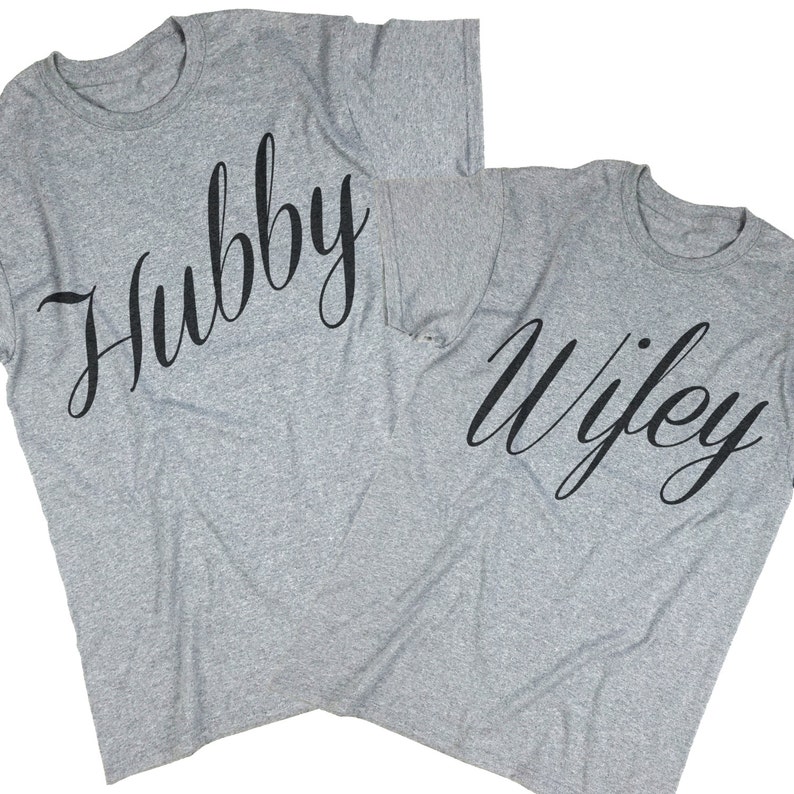 Puede incluir: Dos camisetas grises con las palabras "Hubby" y "Wifey" impresas en fuente cursiva negra.