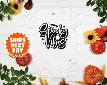 May include: White baby onesie with black text that says "Spooky Vibes" with a ghost and bats.