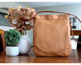 May include: A tan leather shoulder bag with a gold zipper and the text "Noble & Story" embossed on the front.
