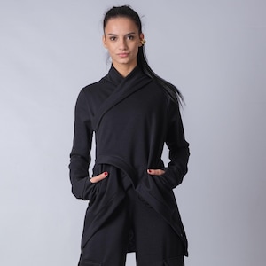 Puede incluir: Una sudadera negra con capucha y diseño envolvente, con mangas largas. La sudadera se combina con pantalones cargo negros y botas negras con cordones.