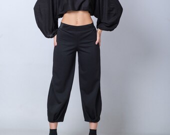May include: A woman wearing a black cropped top with long sleeves and black pants. She is wearing black sunglasses and black sneakers.