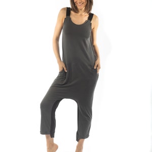 May include: A woman wearing a gray jumpsuit with black straps. The jumpsuit has a loose fit and a wide leg.