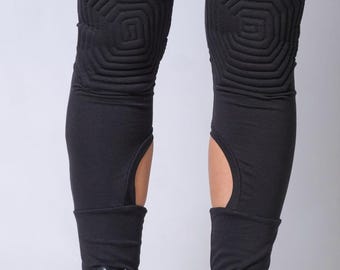May include: Black leggings with quilted geometric knee details and cut-out accents. The leggings are paired with black lace-up boots with zippers. The boots have a thick sole and a rugged appearance, creating a modern, edgy look.
