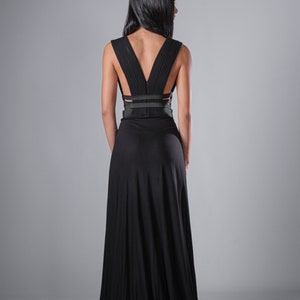 May include: A black maxi dress with a low back and a criss-cross strap detail. The dress is made of a soft, flowing fabric.