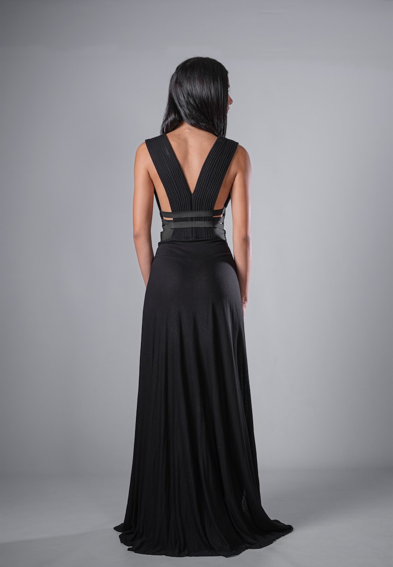 May include: A black maxi dress with a low back and a criss-cross strap detail. The dress is made of a soft, flowing fabric.