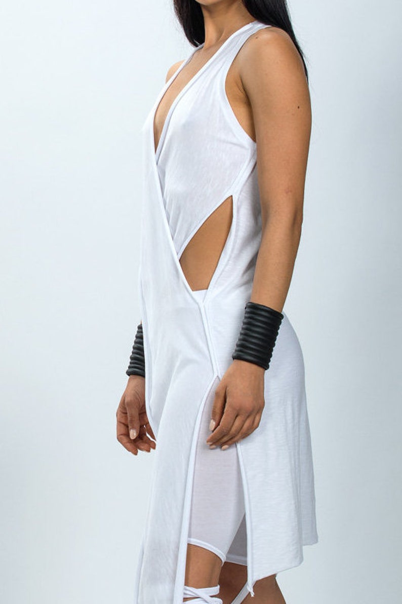 May include: White sleeveless tunic with a deep V-neckline and side slits. The tunic is made of a soft, flowing fabric and has a relaxed fit.
