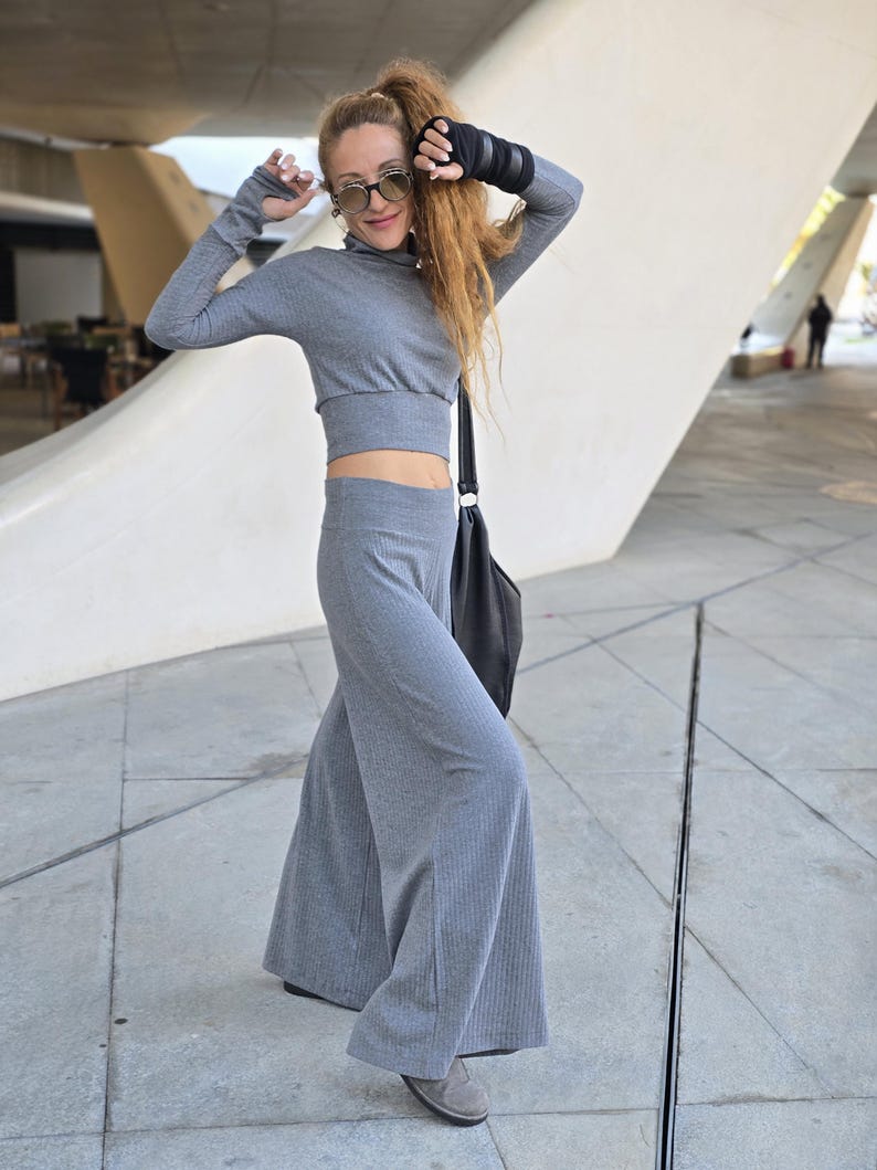 May include: A woman wearing a gray ribbed crop top and matching wide-leg pants. She is wearing round sunglasses and has her hair pulled back in a ponytail.