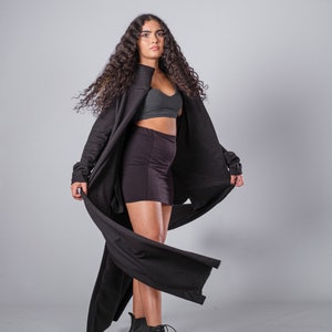May include: A woman wearing a black long-sleeved cardigan with a flowing design, a black mini skirt, and black combat boots. Her hair is long and curly.