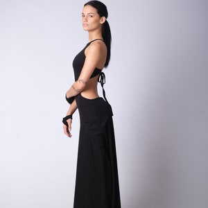 May include: A woman wearing a black maxi dress with a cut-out design and a tie at the back.