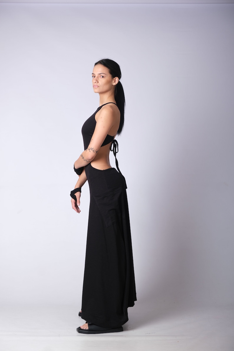 May include: A woman wearing a black maxi dress with a cut-out design and a tie at the back.