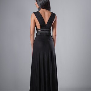May include: A black maxi dress with a V-shaped back and a criss-cross strap detail at the waist.