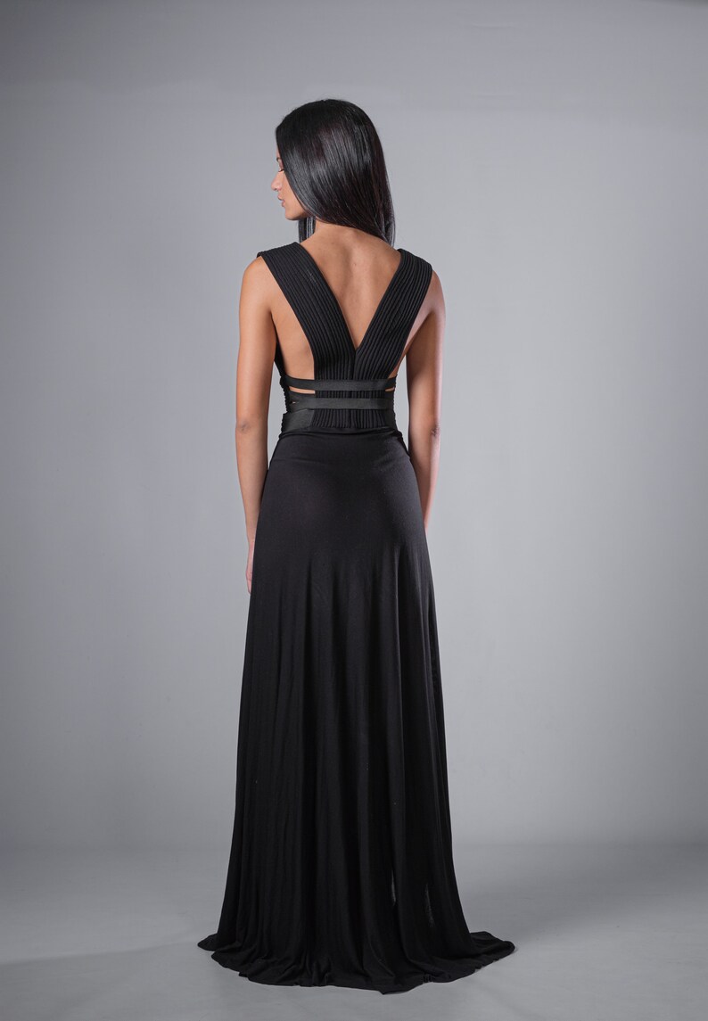May include: A black maxi dress with a V-shaped back and a criss-cross strap detail at the waist.