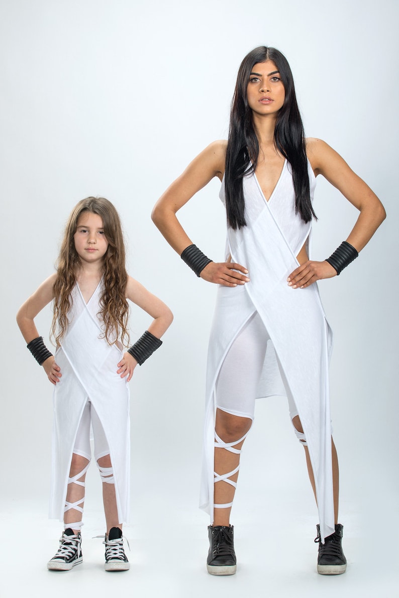 May include: Two people wearing white outfits with black wristbands and white shoes. The outfits have a wrap design and white straps around the legs.