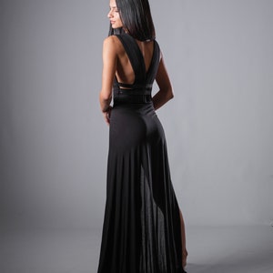May include: A woman wearing a black maxi dress with a low back and a slit in the skirt. The dress has a criss-cross design on the back.