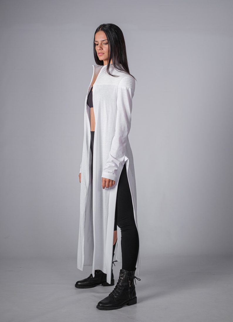 May include: A white long-sleeved shirt with a high neckline and side slits. The shirt is worn over a black bra and black leggings. The person is wearing black lace-up boots.