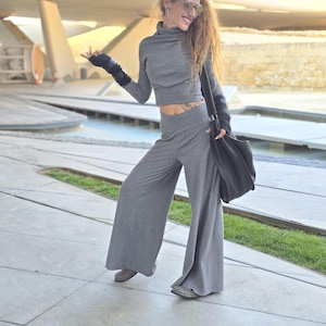 May include: A woman wearing a gray ribbed turtleneck top and matching wide-leg pants. She is wearing sunglasses and has a black bag slung over her shoulder.